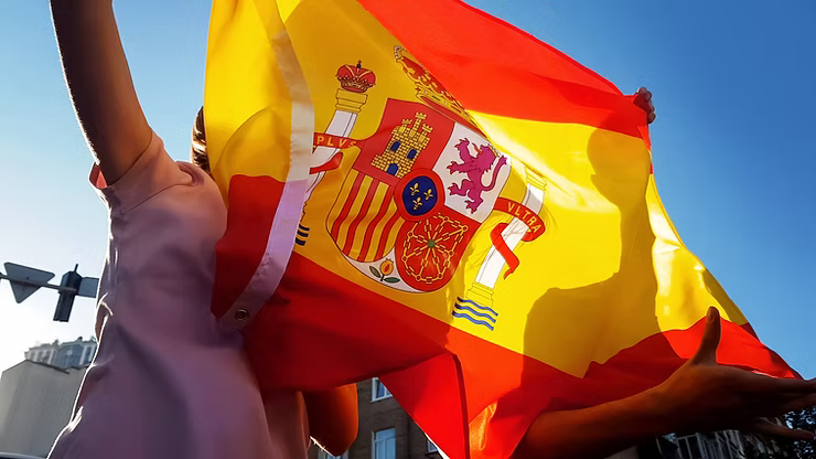 A Spanish flag being held by a person against a blue sky